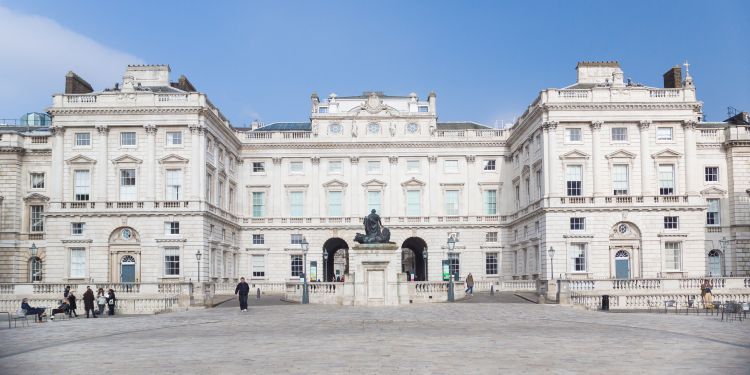 Grand, white buildings with arched entrances and long windows with a statue in front and blue sky