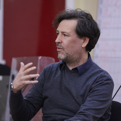 A white man with dark hair in a blue jumper gives a presentation