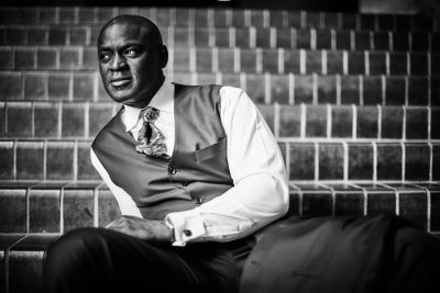 Ola Onabulé wearing a waistcoat and tie, sat on stairs