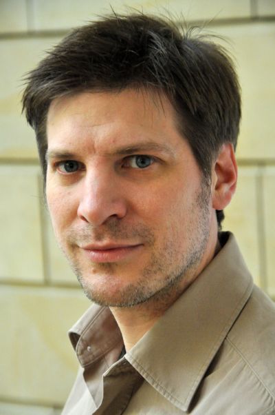 Image of white man with dark hair wearing a beige shirt.